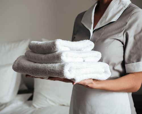 young-hotel-maid-standing-holding-fresh-clean-towels-min young-hotel-maid-standing-holding-fresh-clean-towels-min